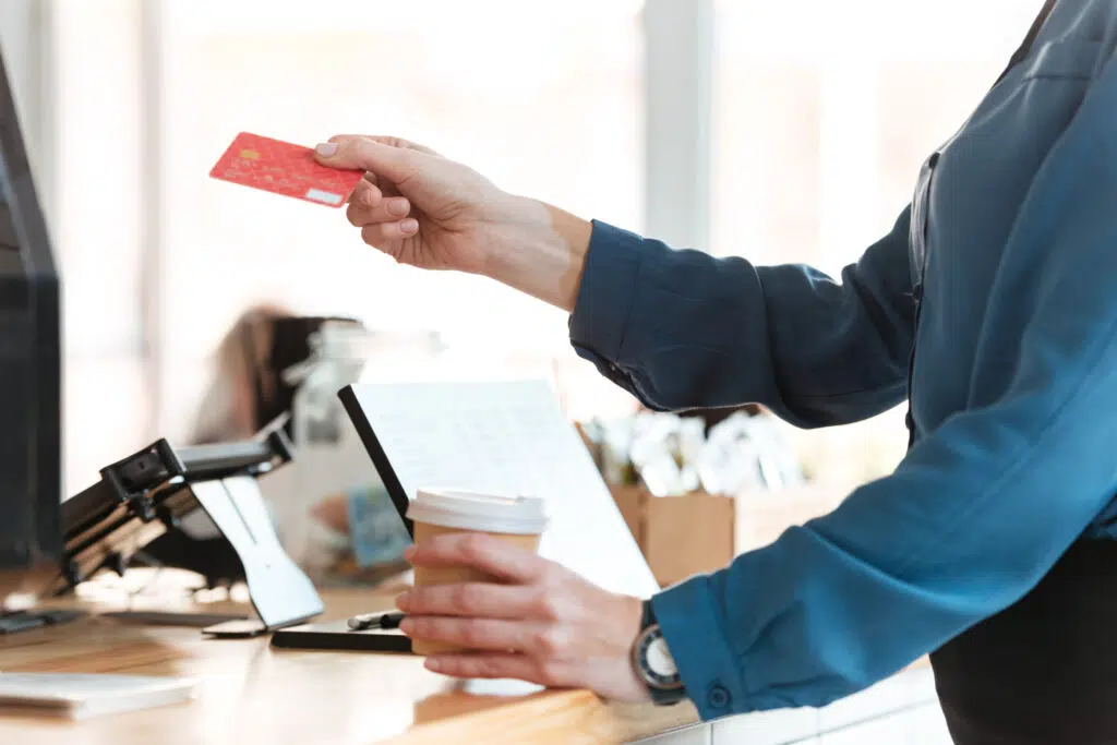 woman in cafe holding credit card and coffee.